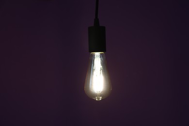 Photo of Glowing light bulb hanging on dark purple background