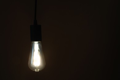 Photo of Glowing light bulb hanging on dark background. Space for text