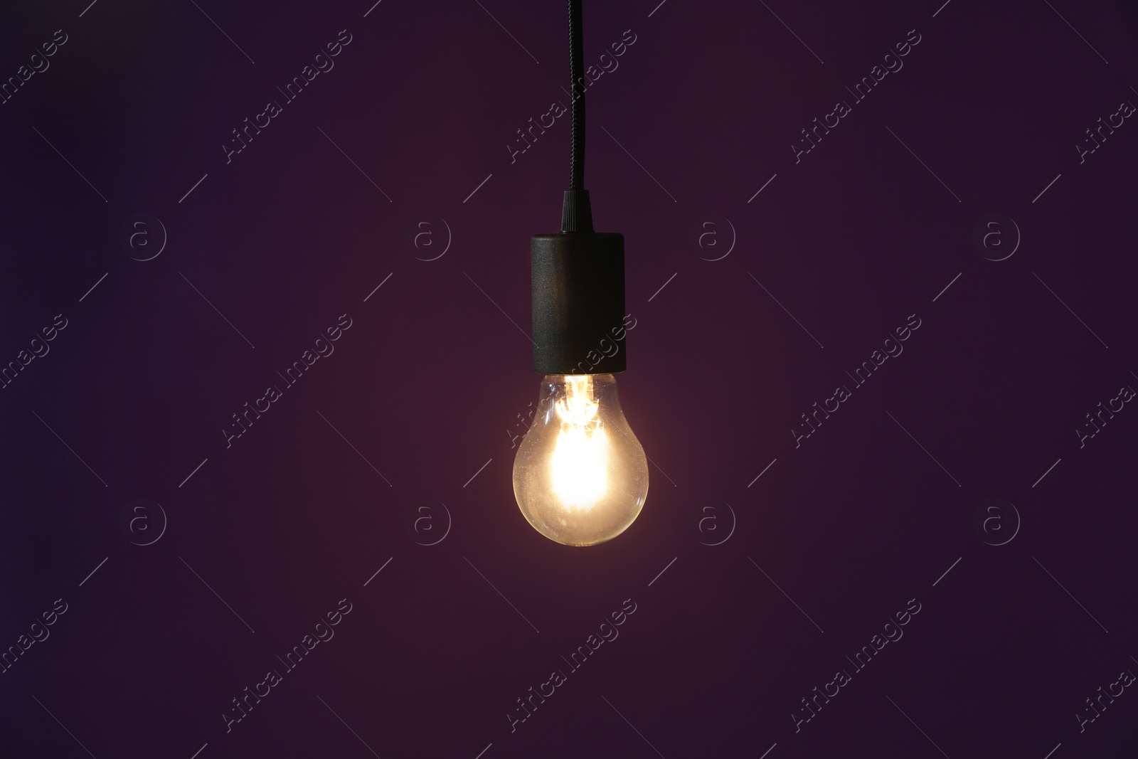 Photo of Glowing light bulb hanging on dark purple background