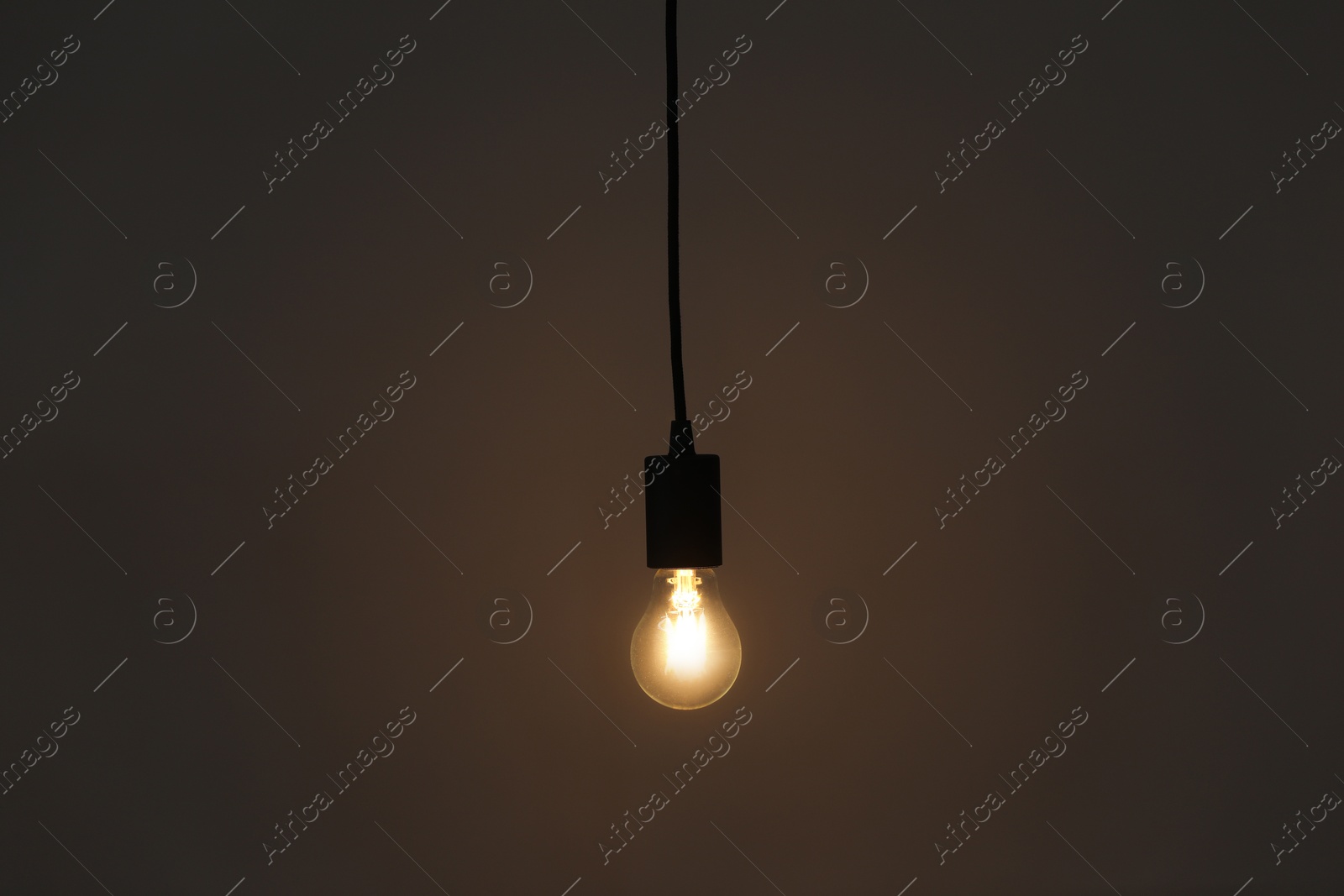 Photo of Glowing light bulb hanging on grey background