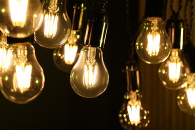 Photo of Glowing light bulbs hanging on dark background, closeup