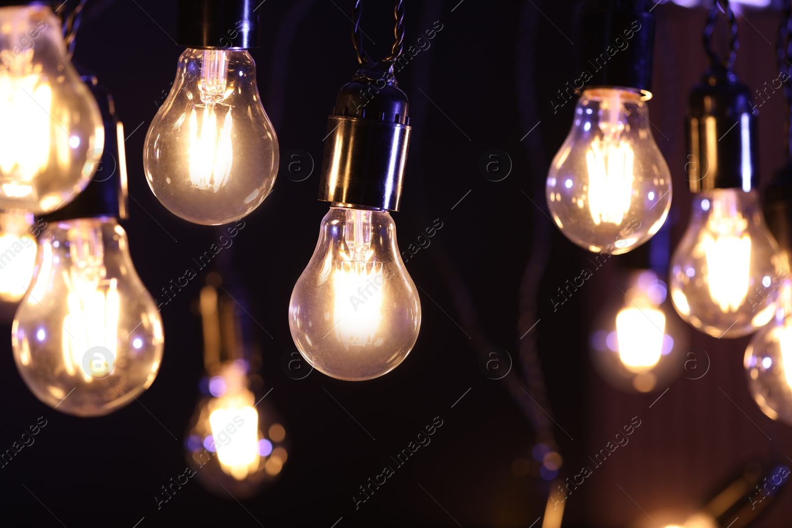 Photo of Glowing light bulbs hanging on dark background, closeup