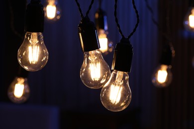 Photo of Glowing light bulbs hanging indoors, closeup view