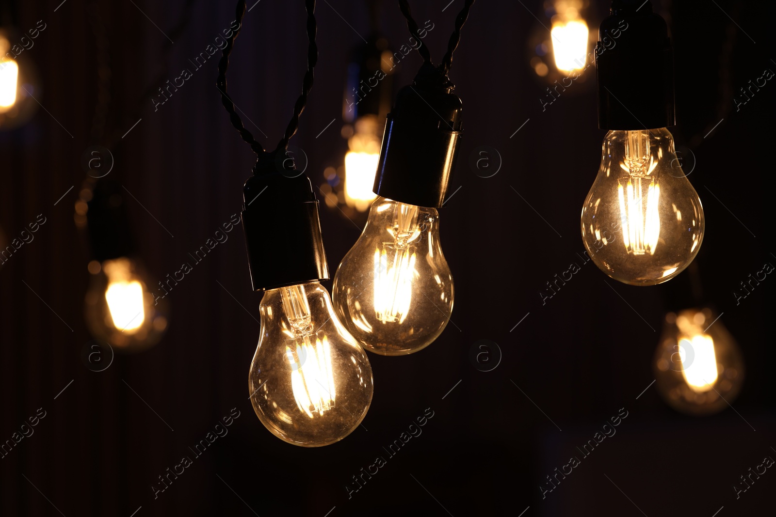 Photo of Glowing light bulbs hanging on dark background, closeup