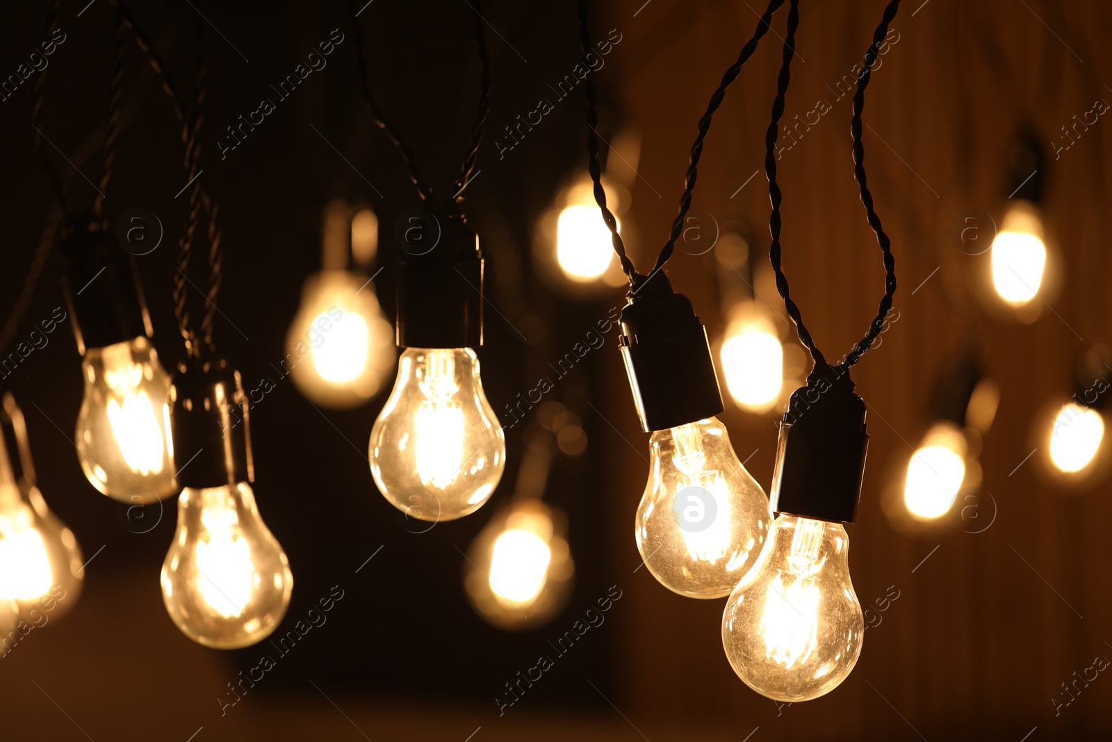 Photo of Glowing light bulbs hanging indoors, closeup view