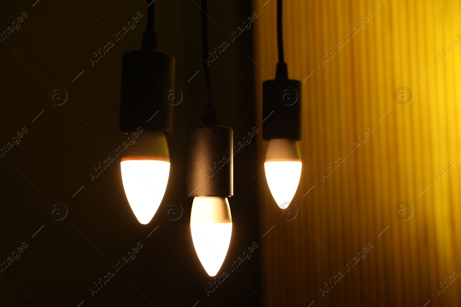 Photo of Glowing light bulbs hanging against color background, closeup