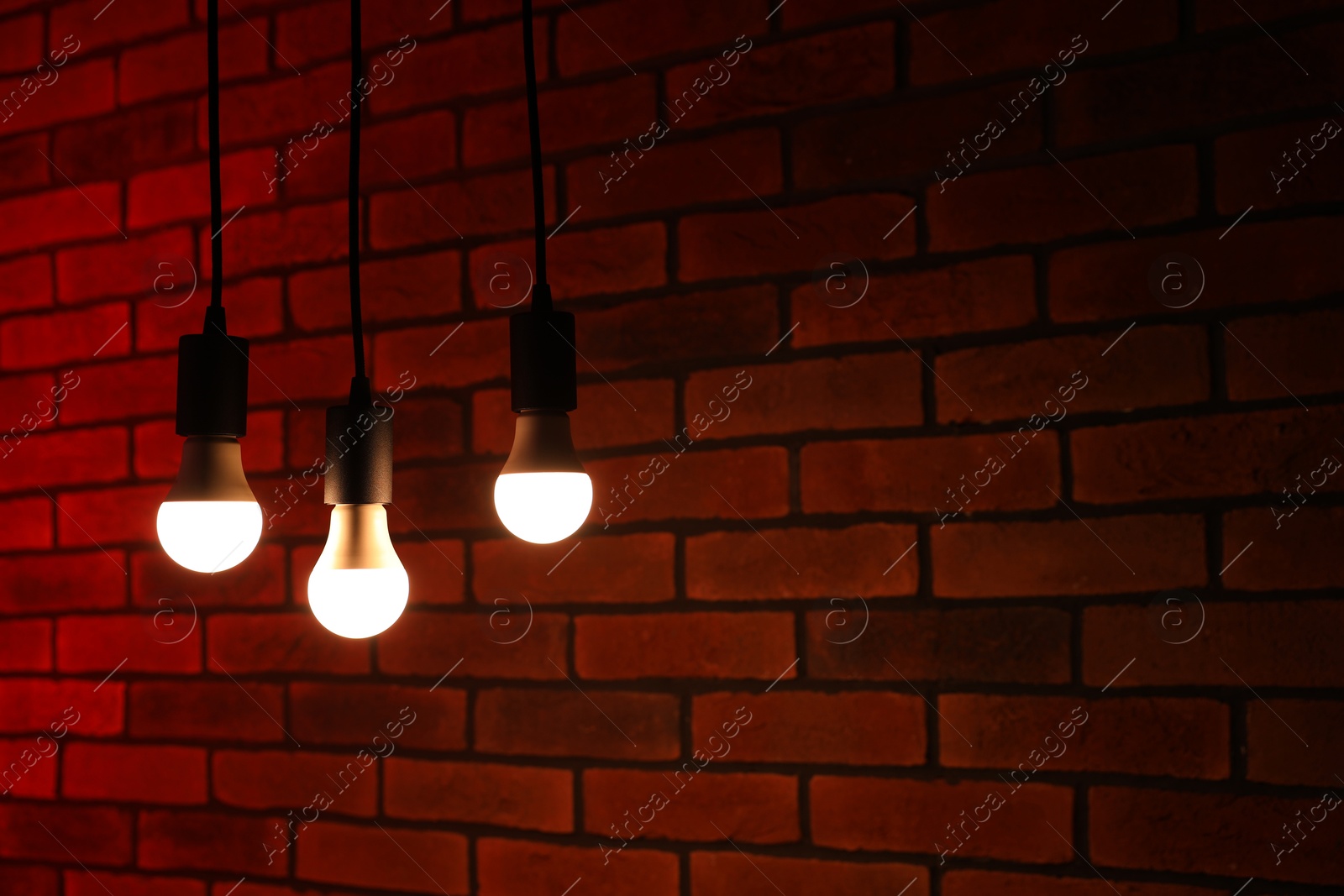 Photo of Glowing light bulbs hanging against brick wall, space for text