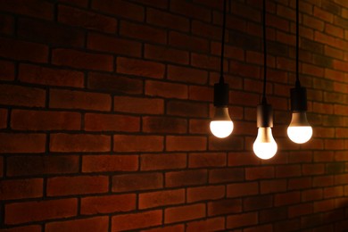 Photo of Glowing light bulbs hanging against brick wall, space for text