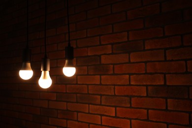 Photo of Glowing light bulbs hanging against brick wall, space for text