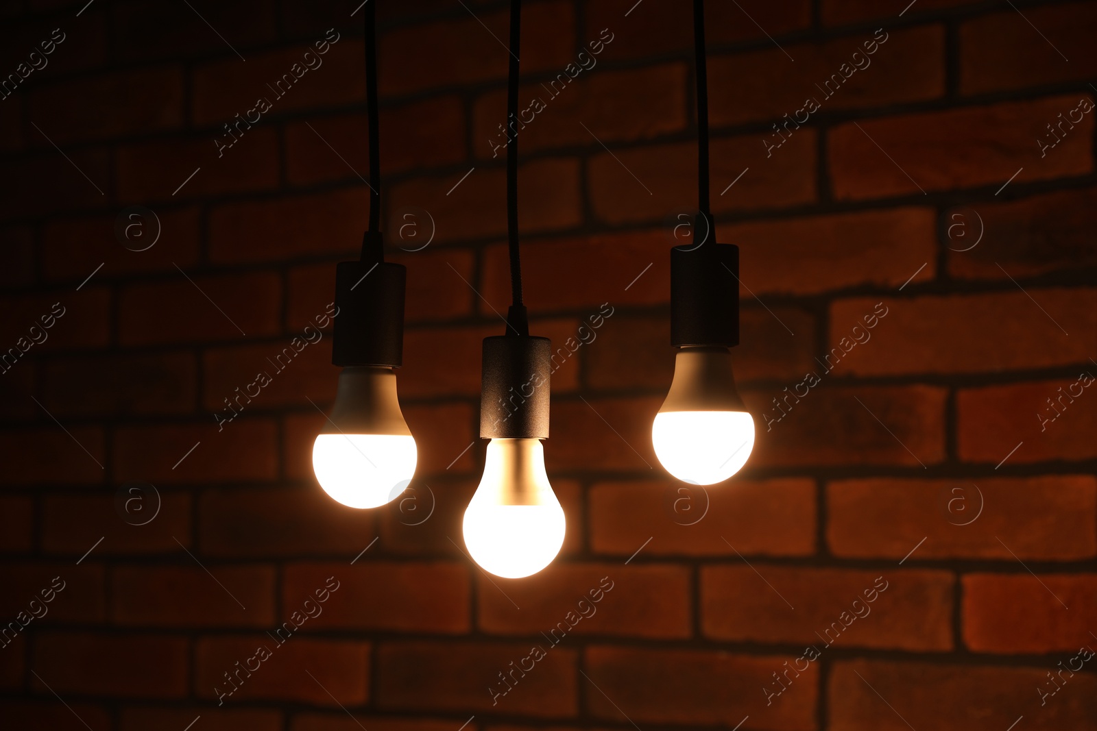 Photo of Glowing light bulbs hanging against brick wall, closeup