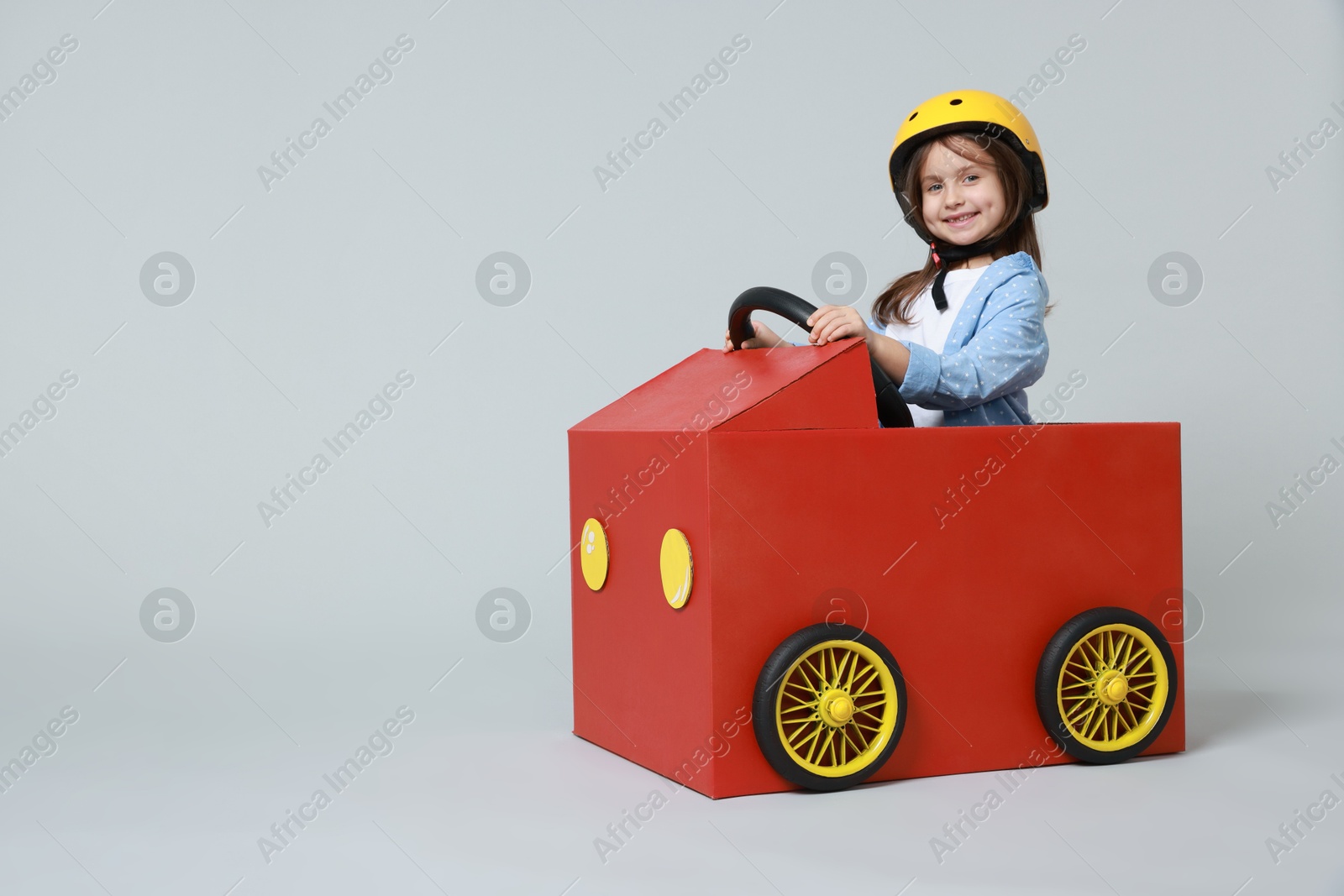 Photo of Little girl driving car made with cardboard on light background. Space for text