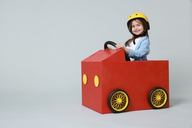 Photo of Little girl driving car made with cardboard on light background. Space for text