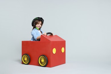 Photo of Little girl driving car made with cardboard on light background. Space for text