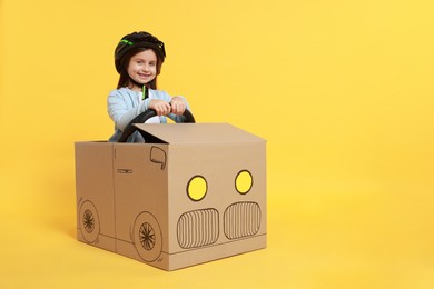 Photo of Little girl driving car made with cardboard on yellow background. Space for text