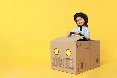 Photo of Little girl driving car made with cardboard on yellow background. Space for text