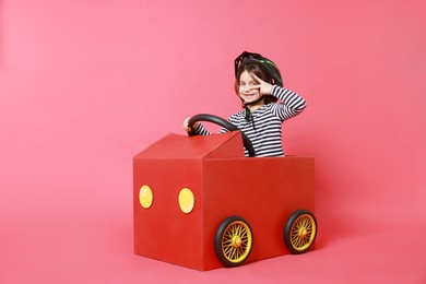 Photo of Little girl showing V-sign while driving car made with cardboard on red background