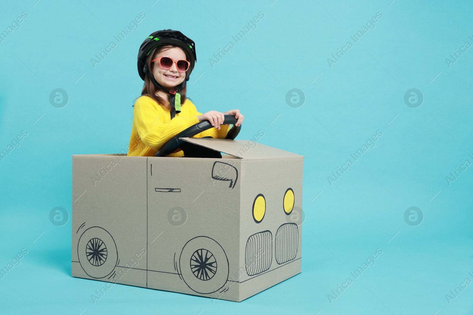 Photo of Little girl driving car made with cardboard on light blue background. Space for text