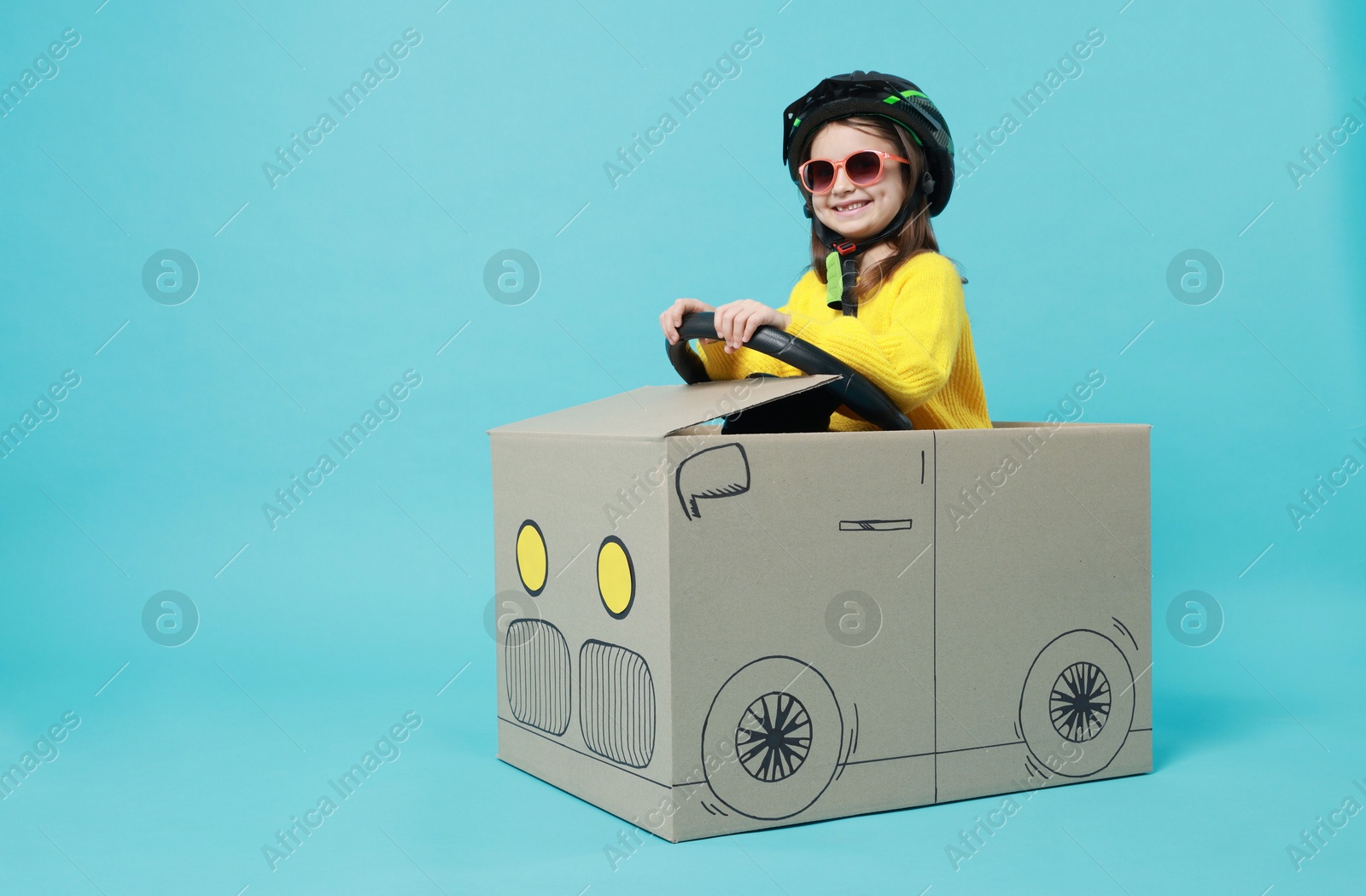 Photo of Little girl driving car made with cardboard on light blue background. Space for text