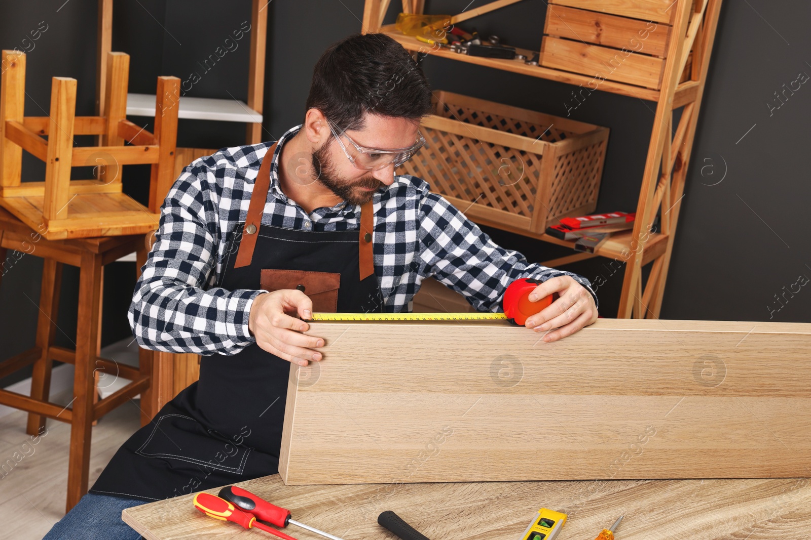 Photo of Relaxing hobby. Man measuring wooden plank with tape at table in workshop