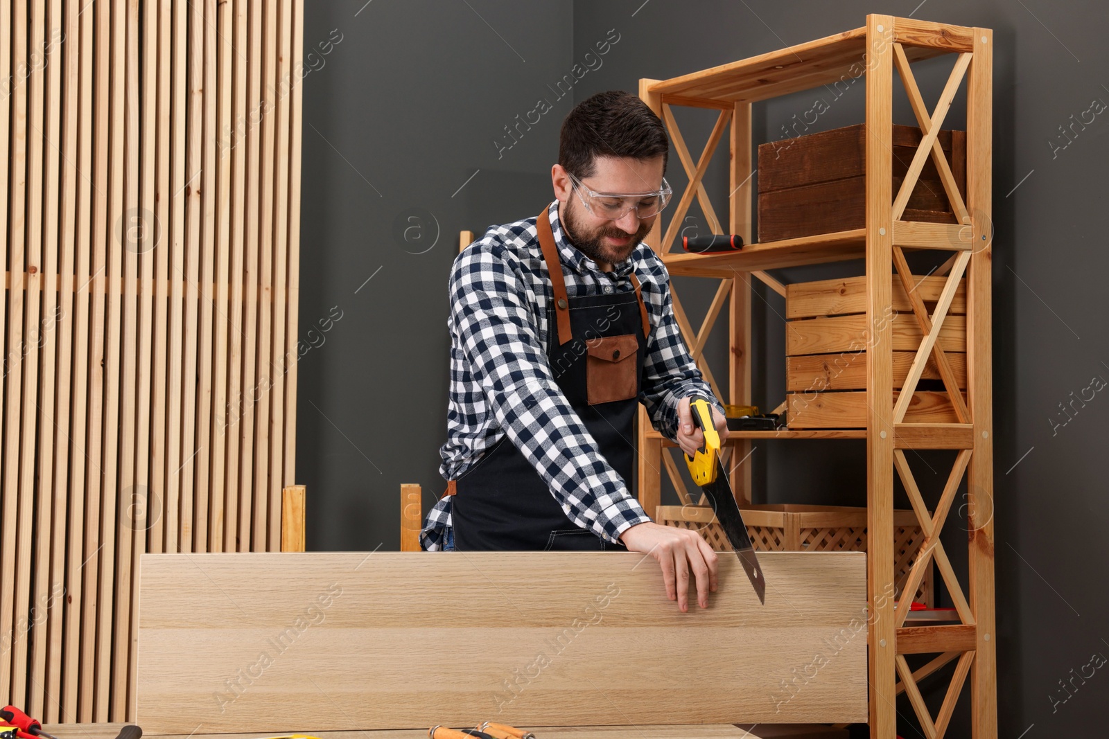 Photo of Relaxing hobby. Man sawing wooden plank at table in workshop