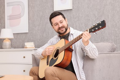 Photo of Relaxing hobby. Smiling man playing guitar on armchair at home