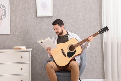 Photo of Relaxing hobby. Man with guitar and book on armchair at home