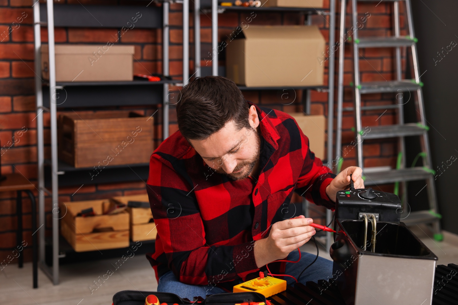 Photo of Relaxing hobby. Man testing deep fryer with multimeter in workshop