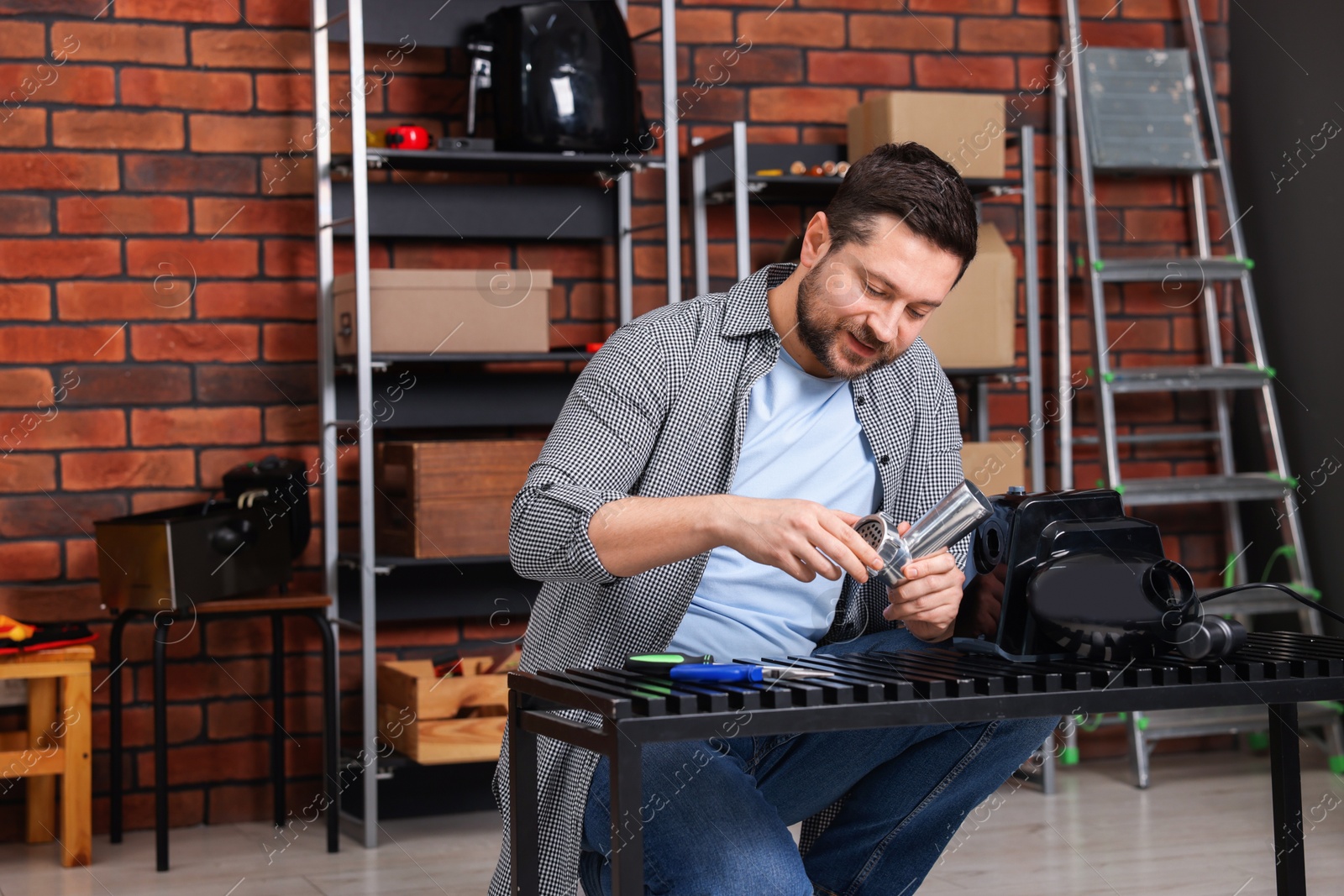 Photo of Relaxing hobby. Man examining parts of electric meat grinder in workshop, space for text