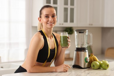 Photo of Weight loss. Woman with glass of healthy shake and measuring tape at white marble table in kitchen