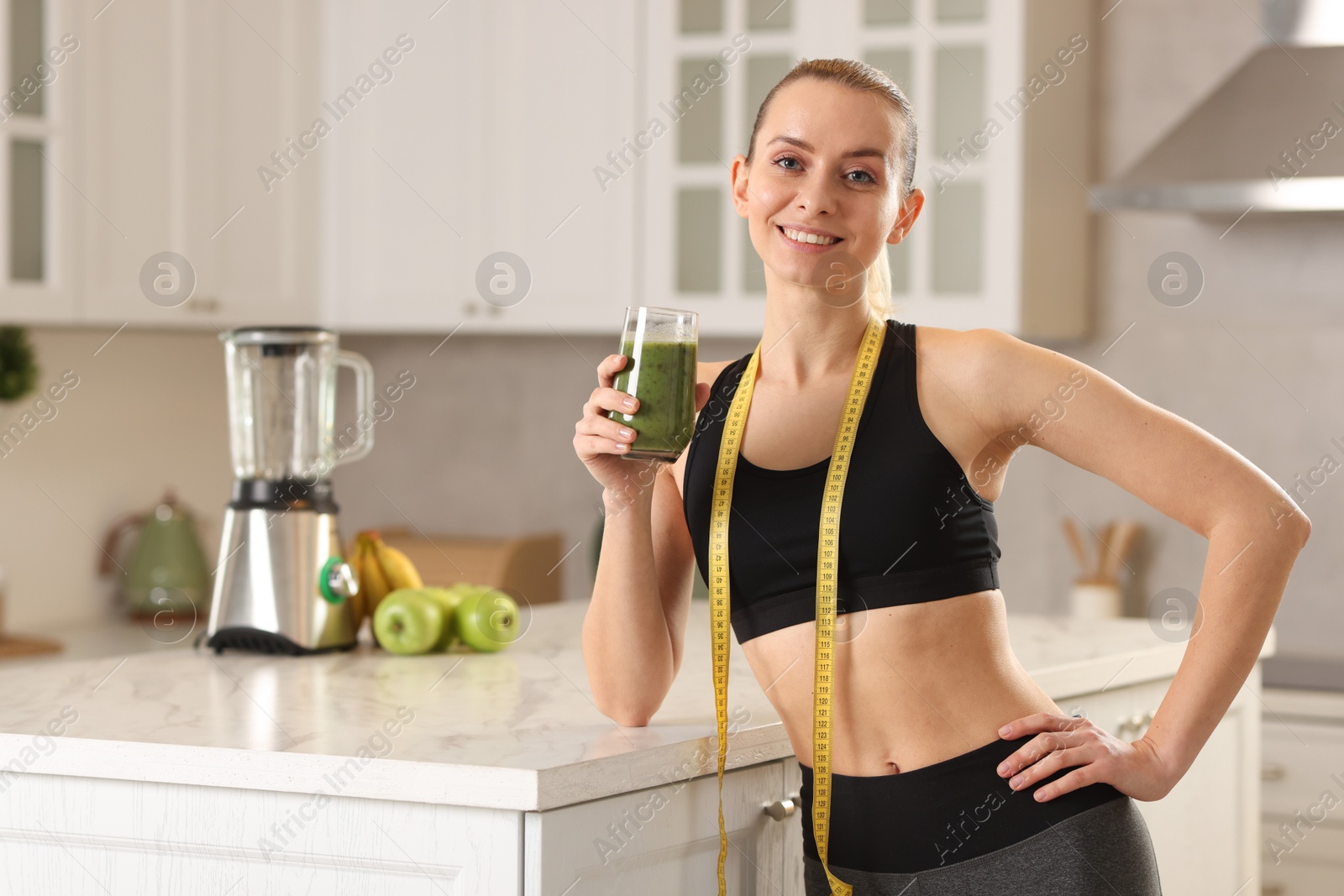 Photo of Weight loss. Woman with glass of healthy shake and measuring tape in kitchen