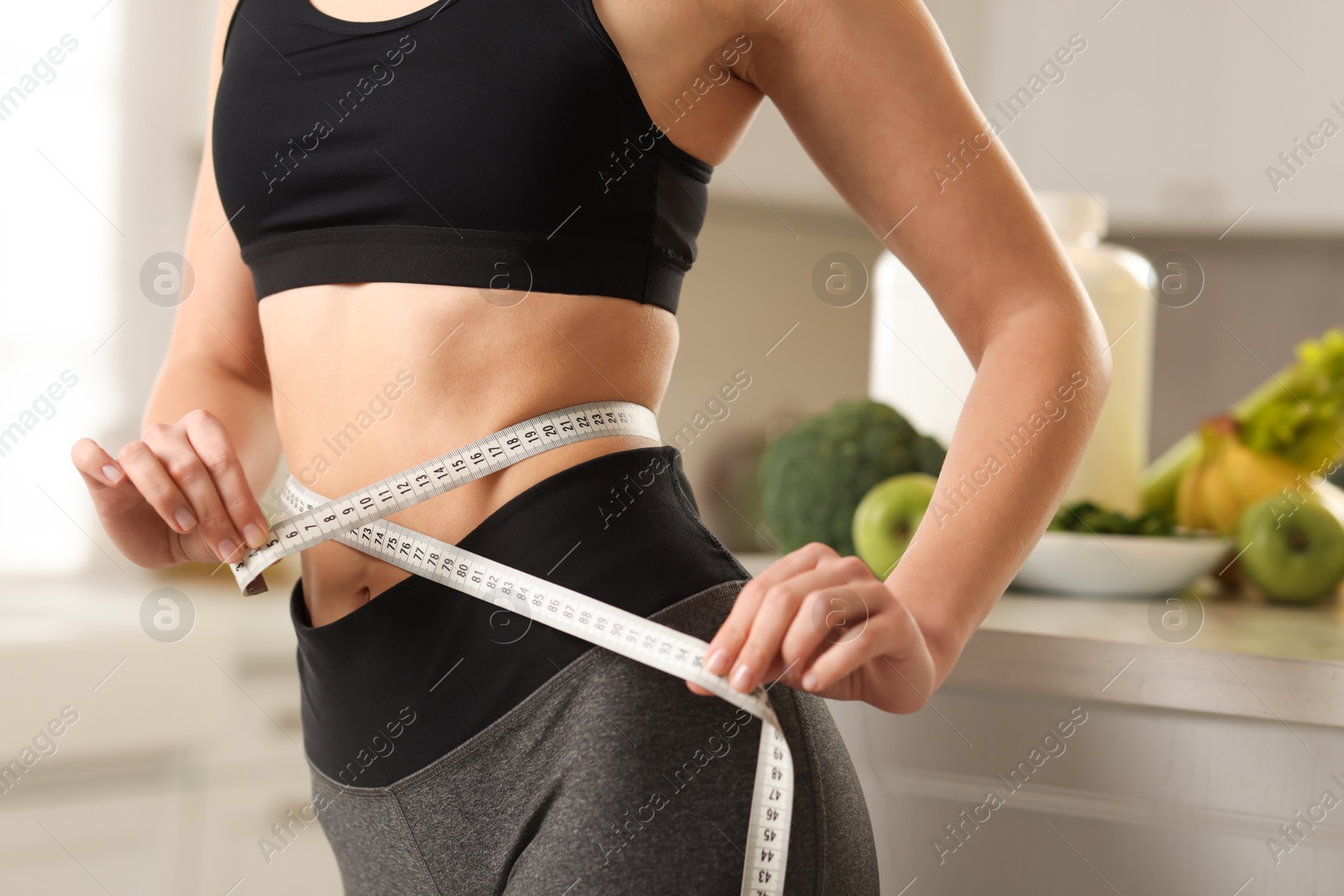 Photo of Weight loss. Woman measuring waist with tape in kitchen, closeup