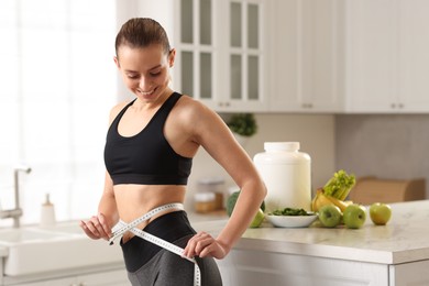 Photo of Weight loss. Woman measuring waist with tape in kitchen