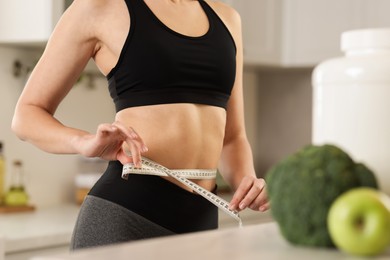 Photo of Weight loss. Woman measuring waist with tape in kitchen, closeup