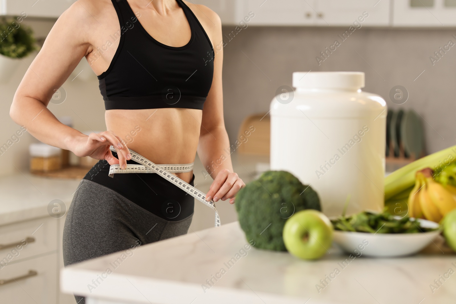 Photo of Weight loss. Woman measuring waist with tape in kitchen, closeup