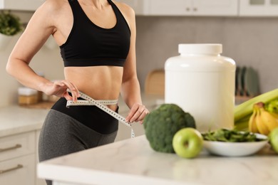 Photo of Weight loss. Woman measuring waist with tape in kitchen, closeup