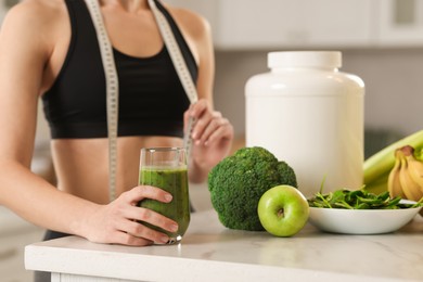 Photo of Weight loss. Woman with glass of healthy shake and measuring tape at white marble table in kitchen, closeup