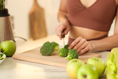 Photo of Weight loss. Woman cutting broccoli for healthy shake at white marble table in kitchen, closeup