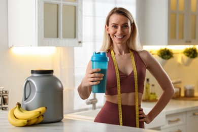 Photo of Weight loss. Woman with shaker of protein and measuring tape in kitchen