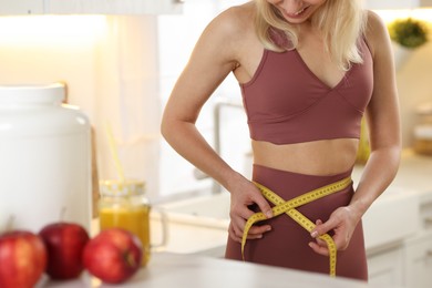 Photo of Weight loss. Woman measuring waist with tape in kitchen, closeup