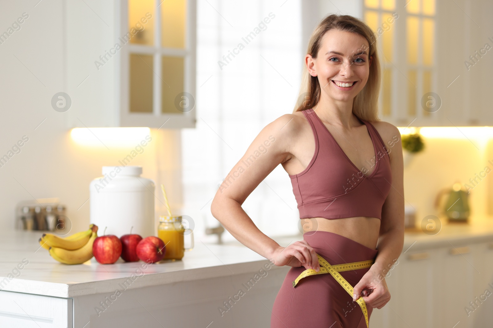 Photo of Weight loss. Woman measuring waist with tape in kitchen