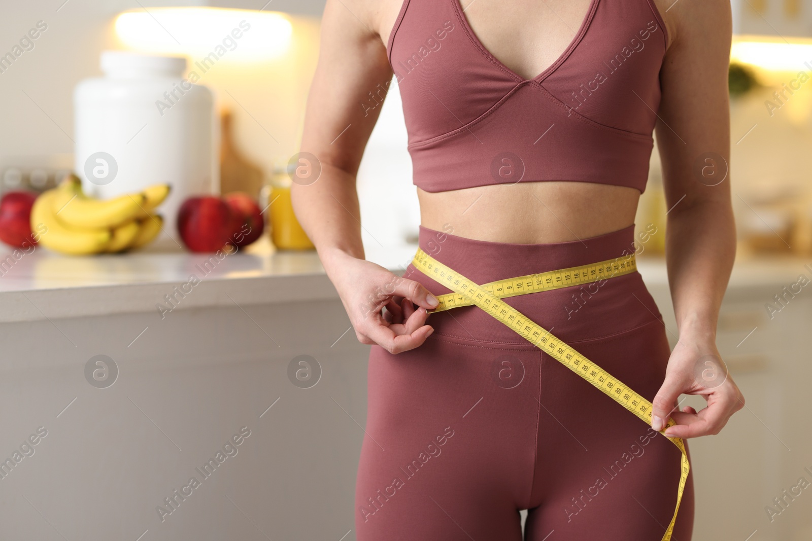 Photo of Weight loss. Woman measuring waist with tape in kitchen, closeup