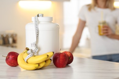 Photo of Weight loss. Woman with tasty shake in kitchen, focus on fresh fruits, jar and measuring tape