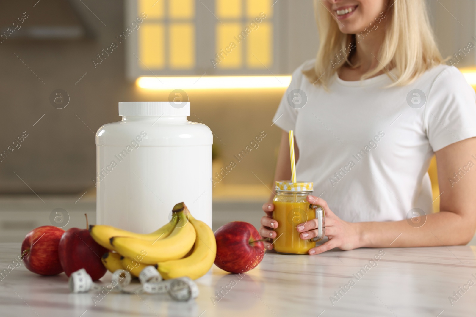 Photo of Weight loss. Happy woman with tasty shake, fresh fruits, measuring tape and jar at white marble table in kitchen, closeup