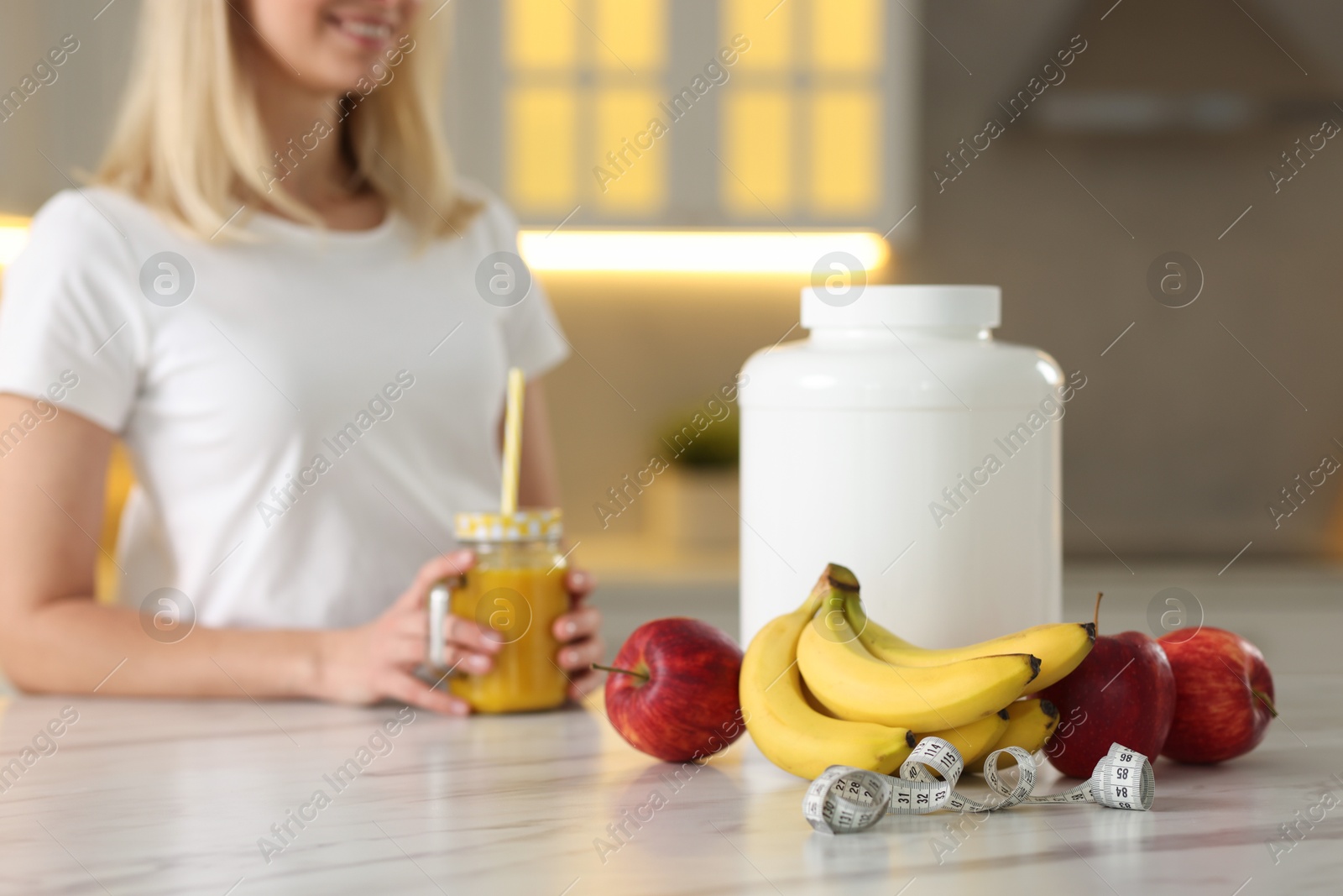 Photo of Weight loss. Happy woman with tasty shake, fresh fruits, measuring tape and jar at white marble table in kitchen, selective focus