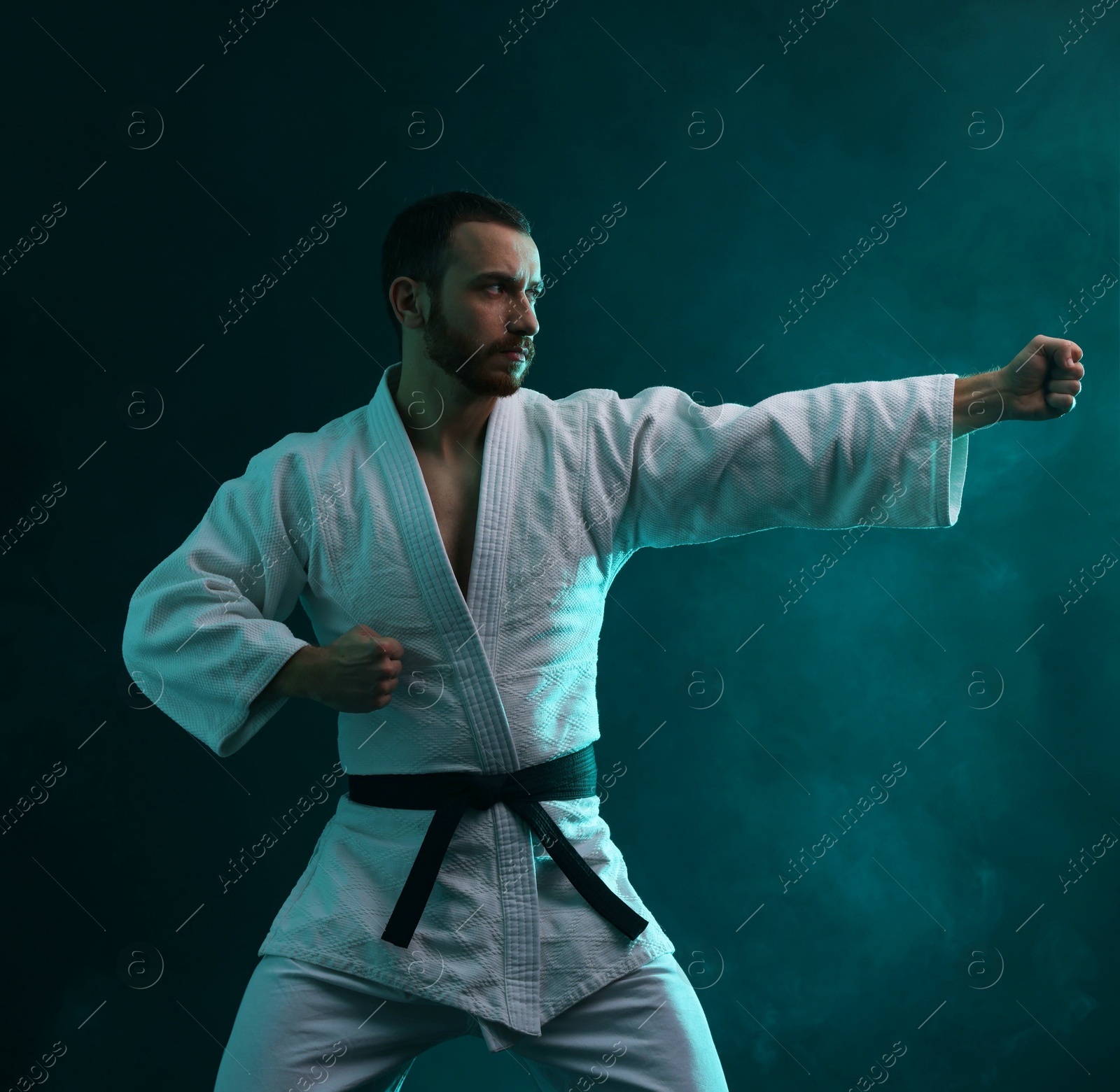 Photo of Man wearing uniform practicing karate in color lights and smoke