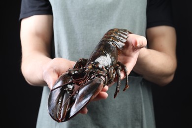 Photo of Man with raw lobster on black background, closeup