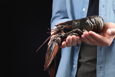 Photo of Man with raw lobster on black background, closeup. Space for text