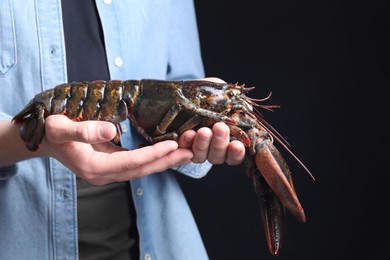 Photo of Man with raw lobster on black background, closeup. Space for text