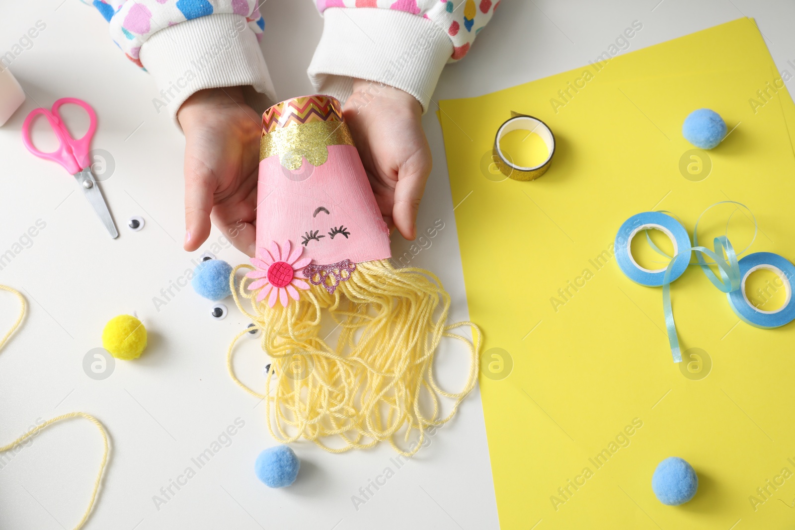 Photo of Little girl with handmade toy at white table, top view. Child creativity and craft