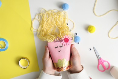 Photo of Little girl with handmade toy at white table, top view. Child creativity and craft